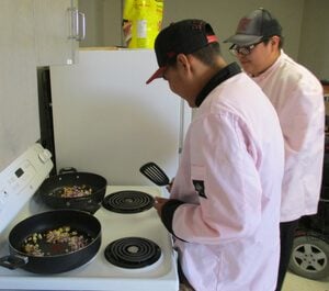 Cooking: 300 x 265 Colton (in back) with classmate Morgan, wearing chef uniforms and cooking at stove
