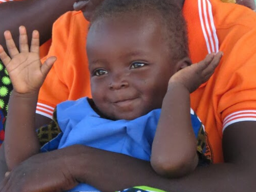 A small baby smiles while throwing up his arms