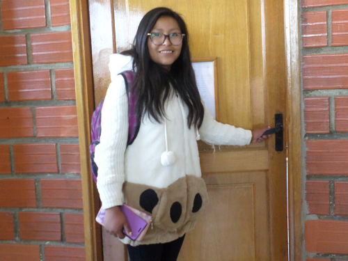 A university student holds books and smiles for the camera