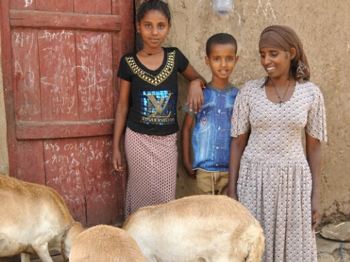 A mother and her two children smile and pose with their sheep