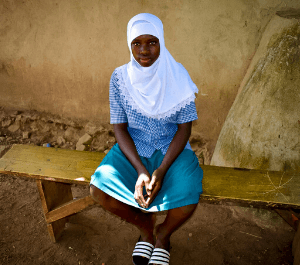 An adolescent girl sits on a bench and looks to the camera