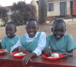 Three girls eating lunch on a bench and smiling for the camera