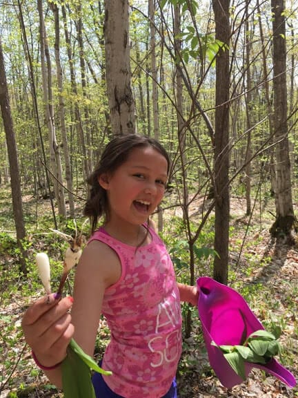 A young girl smiling holding fresh leeks she picked from the garden