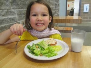 A young girl eats a salad and smiles for the camera