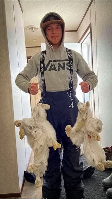 A young man stands holding rabbits he's trapped