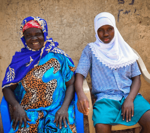 A woman and her daughter sit in front of their home in chairs, posing for the camera