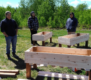 A group of young men pose with wooden flower and vegetable gardens that they've built for the community garden