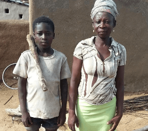 A teenage boy stands next to his mother in front of their house, posing for the camera