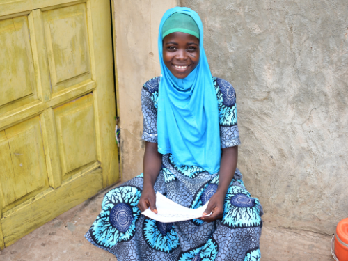 a young girl sits on the pavement in front of her home holding a notebook