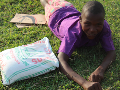 A child lies down in the grass smiling next to a bad of flour