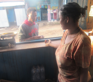 a woman behind a stall sells products to a young man