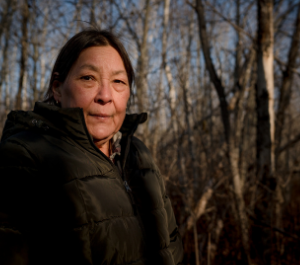 an elder stands in a forest, looking into the camera