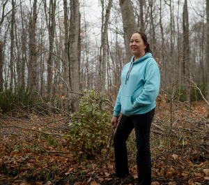 a woman stands in a forest, smiling for the camera