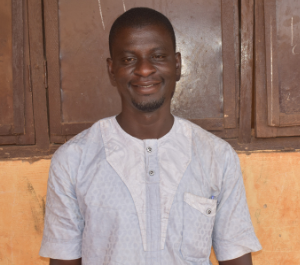 a smiling man stands in front of a wooden cupboard
