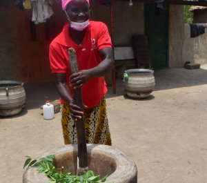 a woman pounds leaves in a giant stone pot