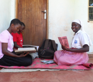 three young girls sit holding workbooks, doing homework