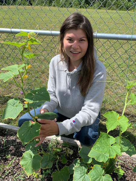 a young woman kneels next to a cucumber plant