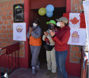 three women in masks stand in front of a community centre