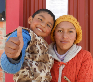 a woman holds a child in her arms who is giving the camera a thumbs up