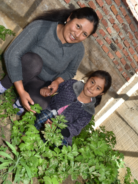 a mom and her young daughter crouching in a garden