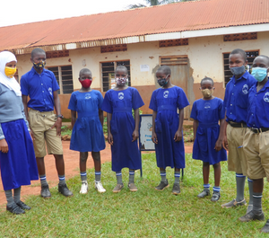 A group of school children wearing masks standing in front of a school