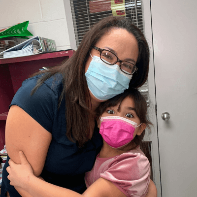 Holly, left and her daughter Josie hug. They are wearing masks, but their eyes are smiling. 