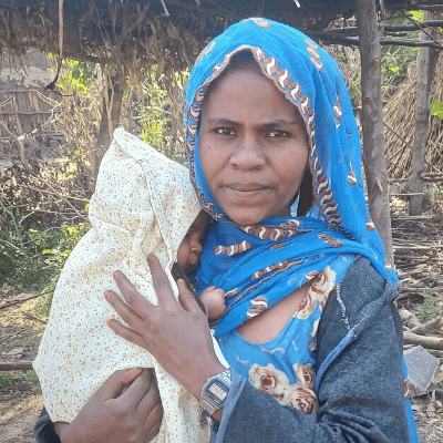 Neima holds her small baby in an outdoor setting