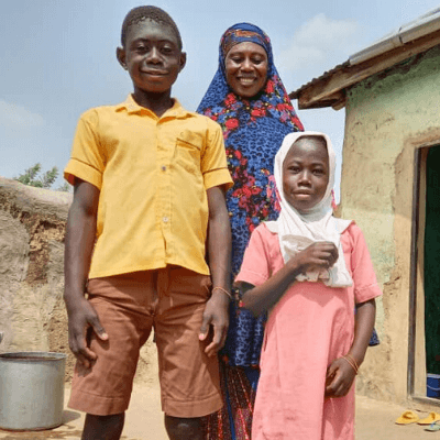 Sikeina (in the back) stands in front of the house with her children. 