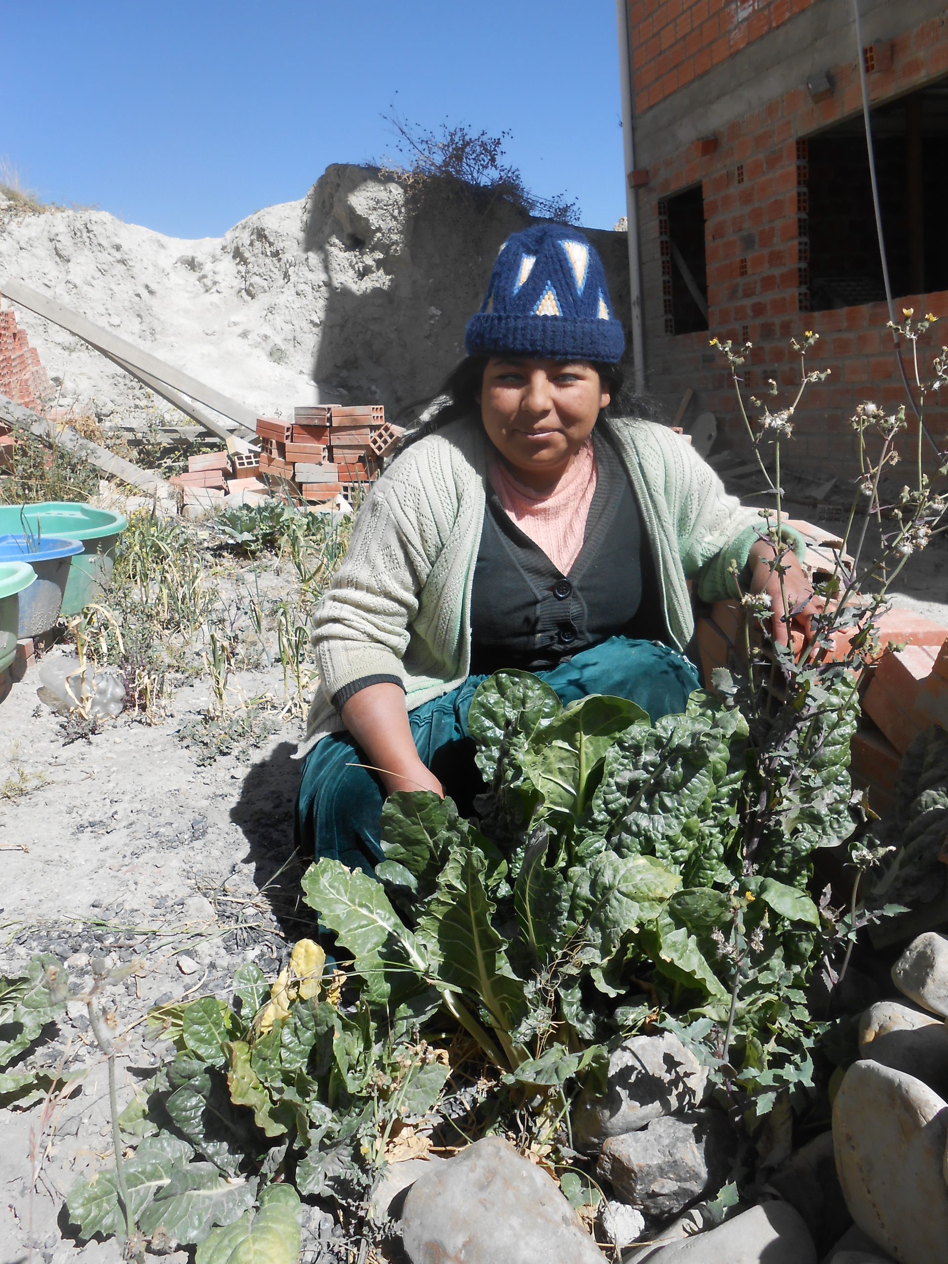 Viviana stands over her garden, showing off vegetables. 