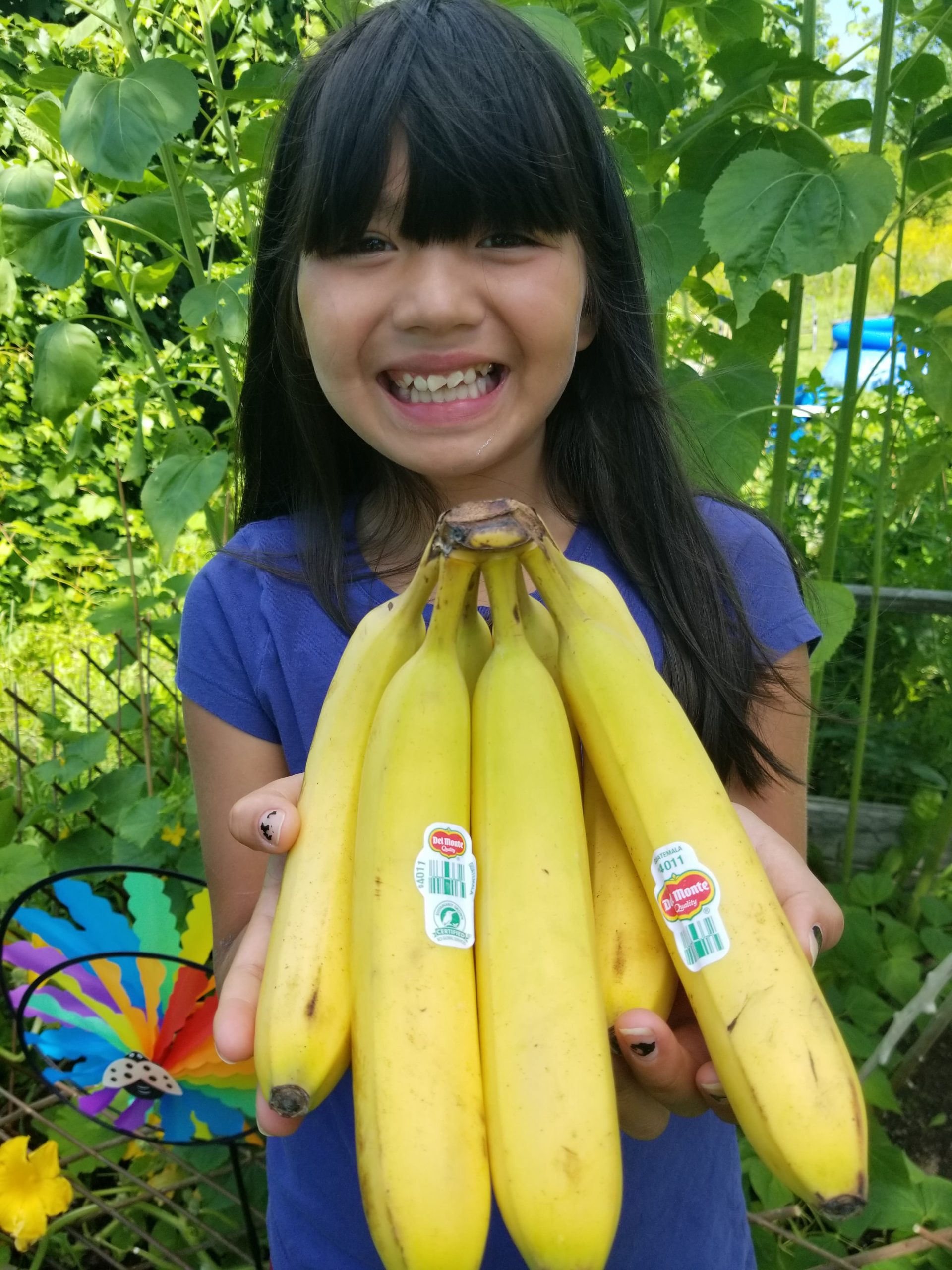 Bella stands in a garden with bananas, smiling into the camera. 