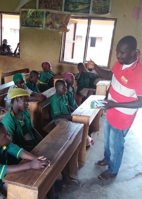 a Ghanaian man stands in a classroom in front of students