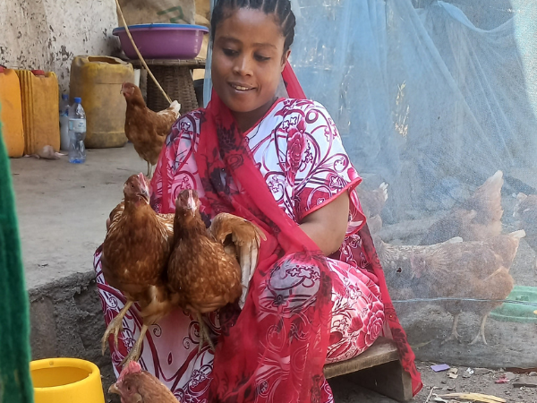 a woman stoops in the ground holding her chickens in her arms