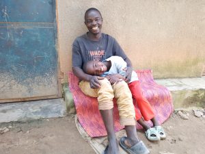 a little girl smiles and rests her head in her father's lap as they sit outside their home