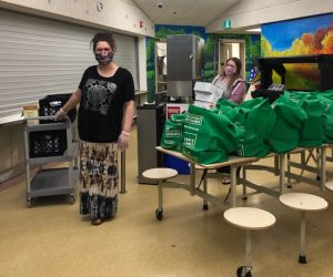 two women in masks standing with bags of food to give to community members