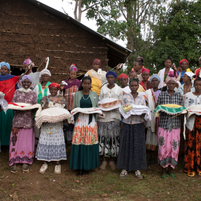 a group of women stand holding their weaving and sewing, smiling
