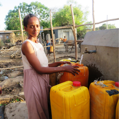 a woman stands with water basins and a tap