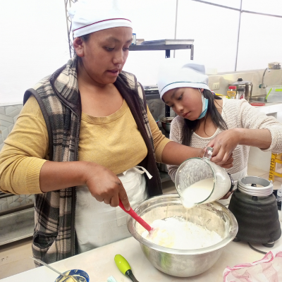 a mother and daughter stir the same mixing bowl in an industrial kitchen