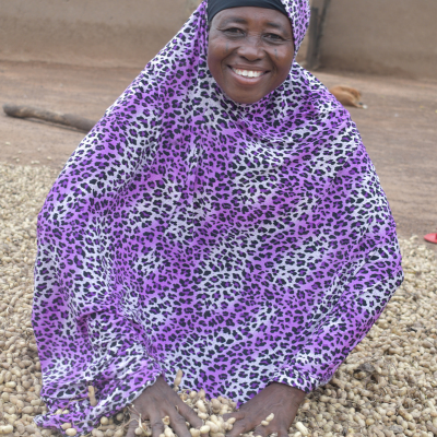 a woman smiles as she kneels in her harvest peanut crop