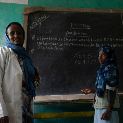 a woman and a girl stand at a classroom chalkboard