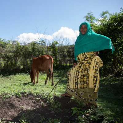 a woman smiles in her field with a cow behind her