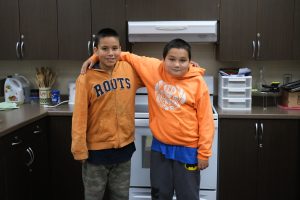 two boys stand smiling with their arms around one another