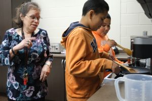 a woman stands in a kitchen with two boys, cooking