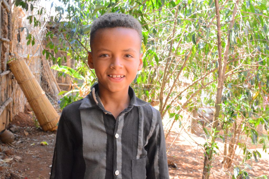 a little boy smiles for the camera in front of trees