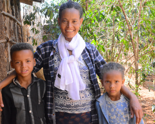 a mom stands smiling with her arms around her children