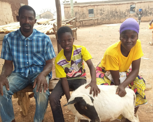 a mom and dad sit with their son, while holding their family goat