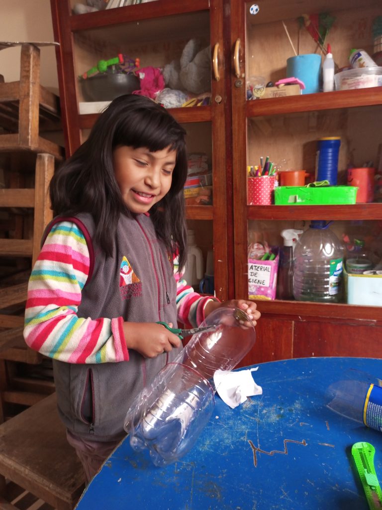 a little girl smiling while cutting into a pop bottle