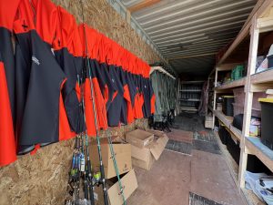 fishing coats and wader pants along with fishing poles on the wall
