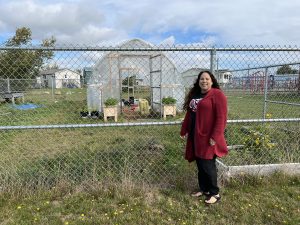 a woman stands in front of a greenhouse garden structure