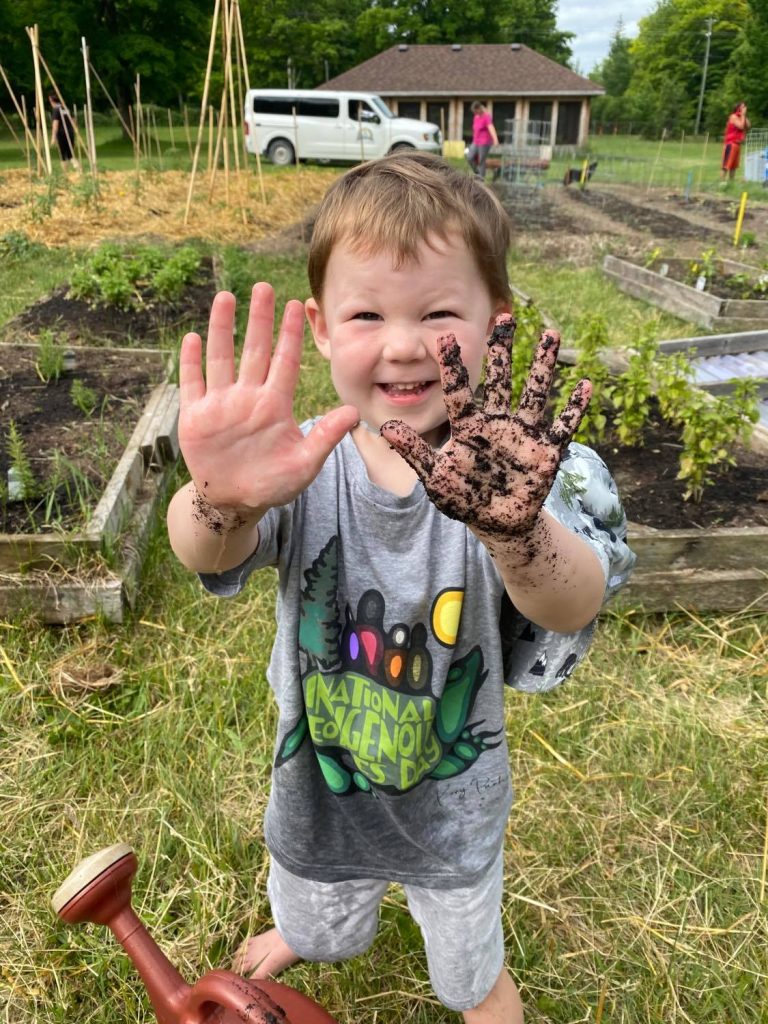 a little boy smiles proudly with dirt on his hands