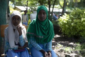 two girls in hijabs sit on chairs, listening to the teacher speak